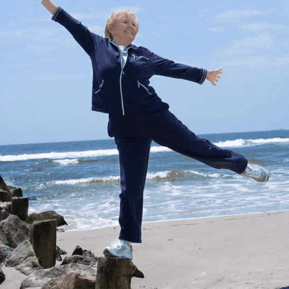 Adulta mayor practica equilibrio sobre una pierna junto al mar